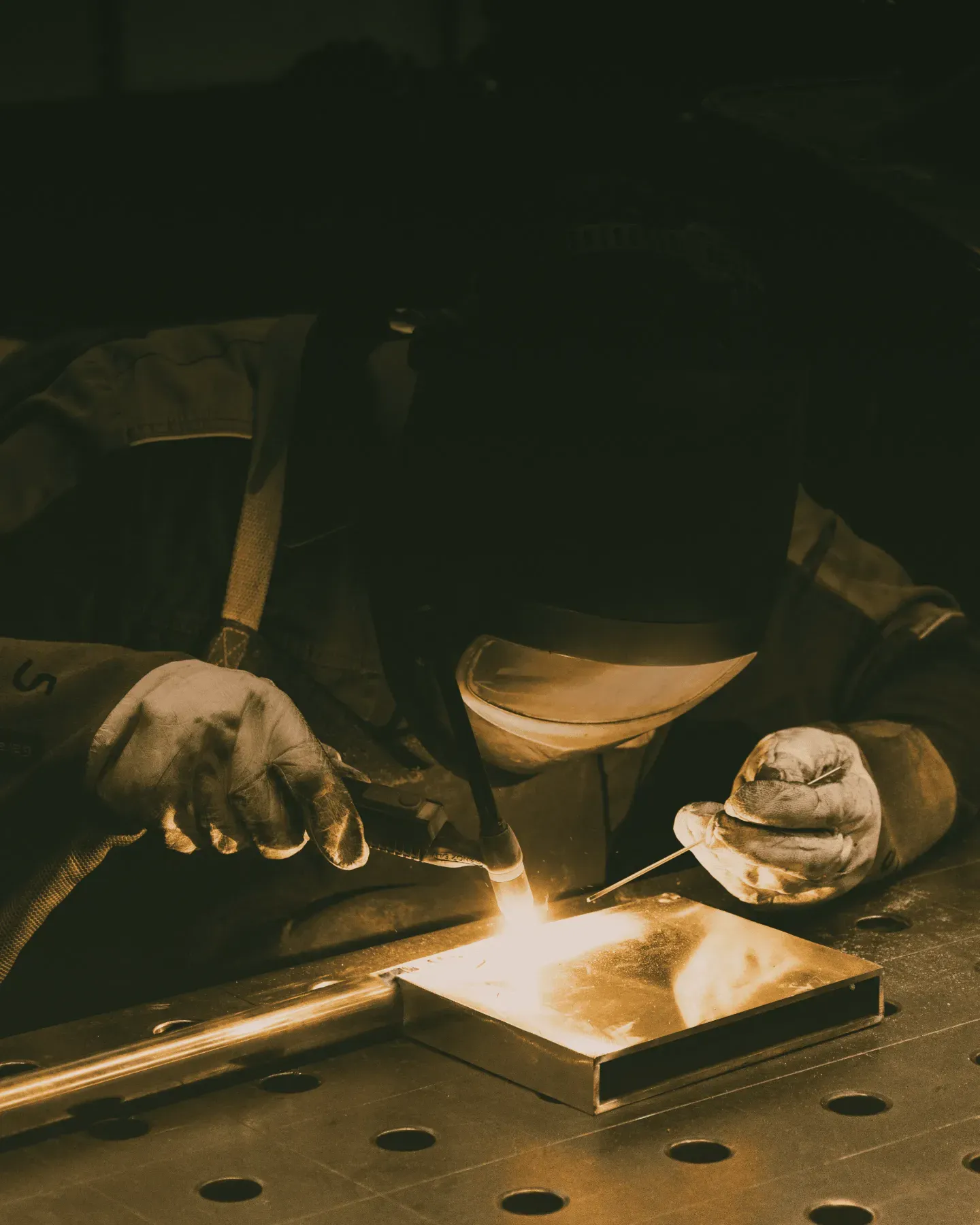 Welder in protective gear sparks bright flame while joining metal pieces.