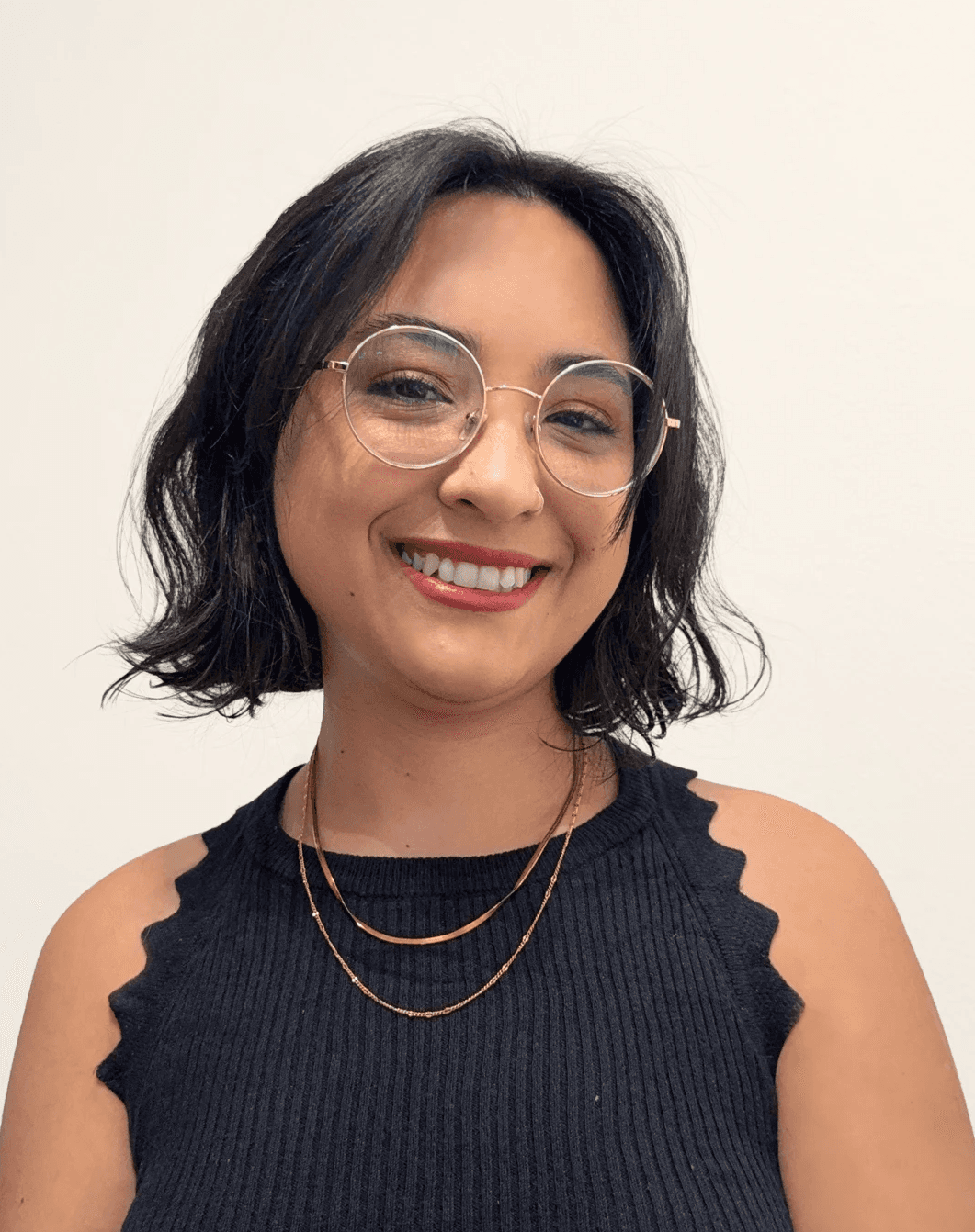 Retrato profesional de Nazarena Roldán con lentes redondos y vestimenta negra, proyectando una imagen cercana y profesional sobre fondo blanco.