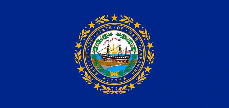 The New Hampshire state flag displays a ship on blue water with a rising sun, surrounded by a wreath and stars, symbolizing history and independence.