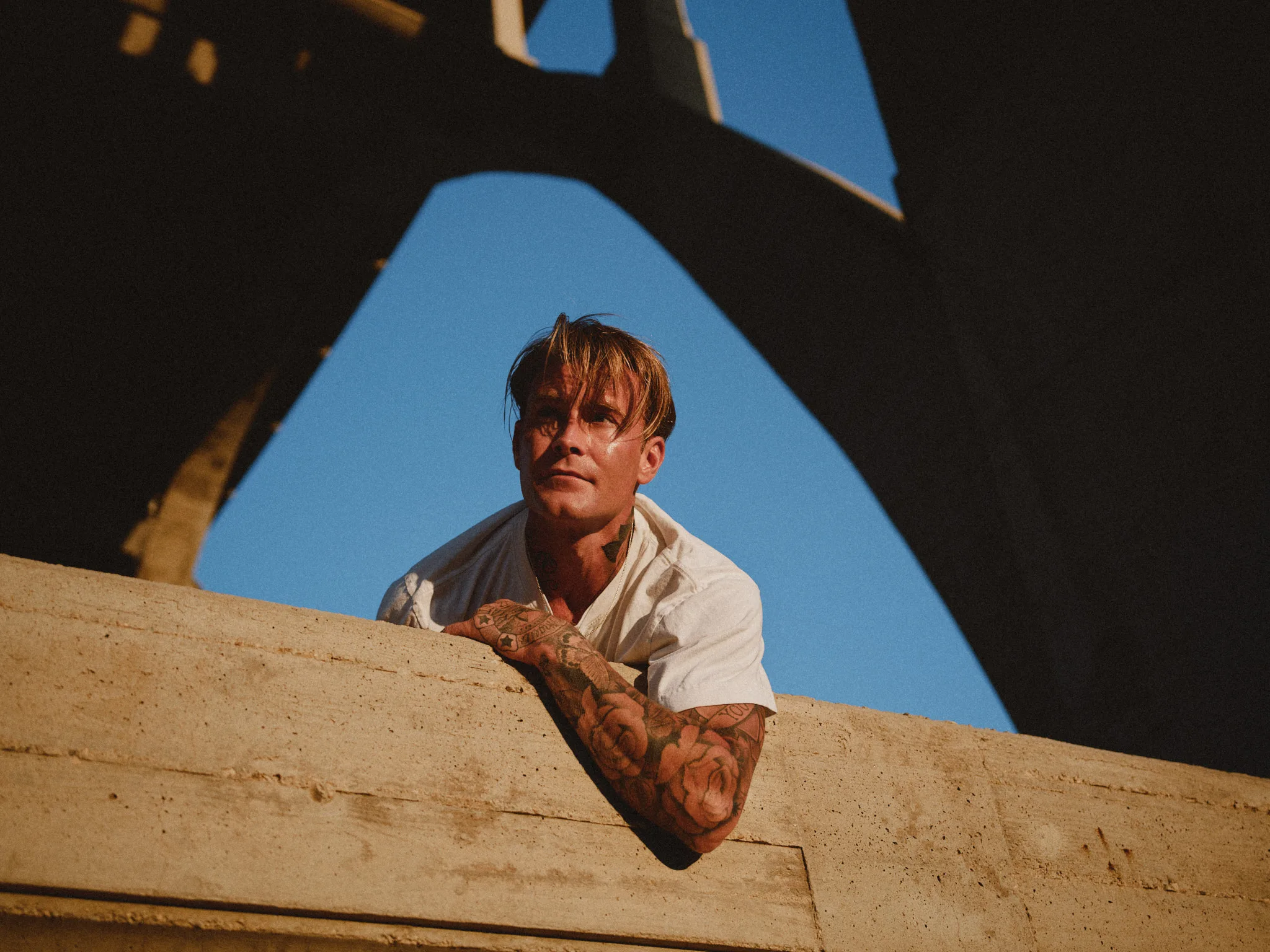 tattooed man leaning over concrete ledge — portrait photography by Tom Kubik