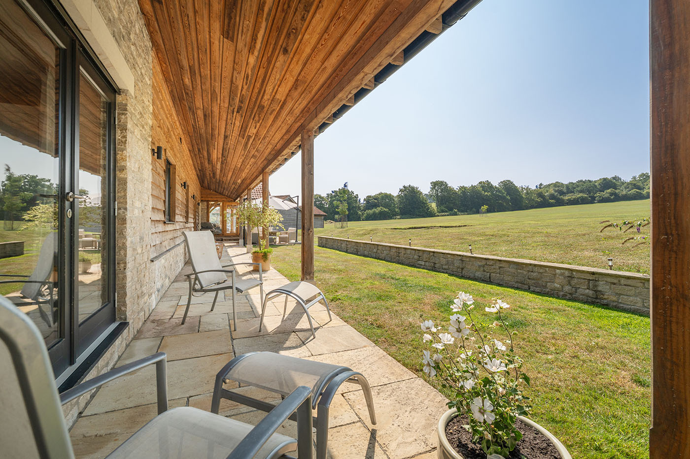 Shaded outdoor terrace with seating overlooking open countryside and lawn