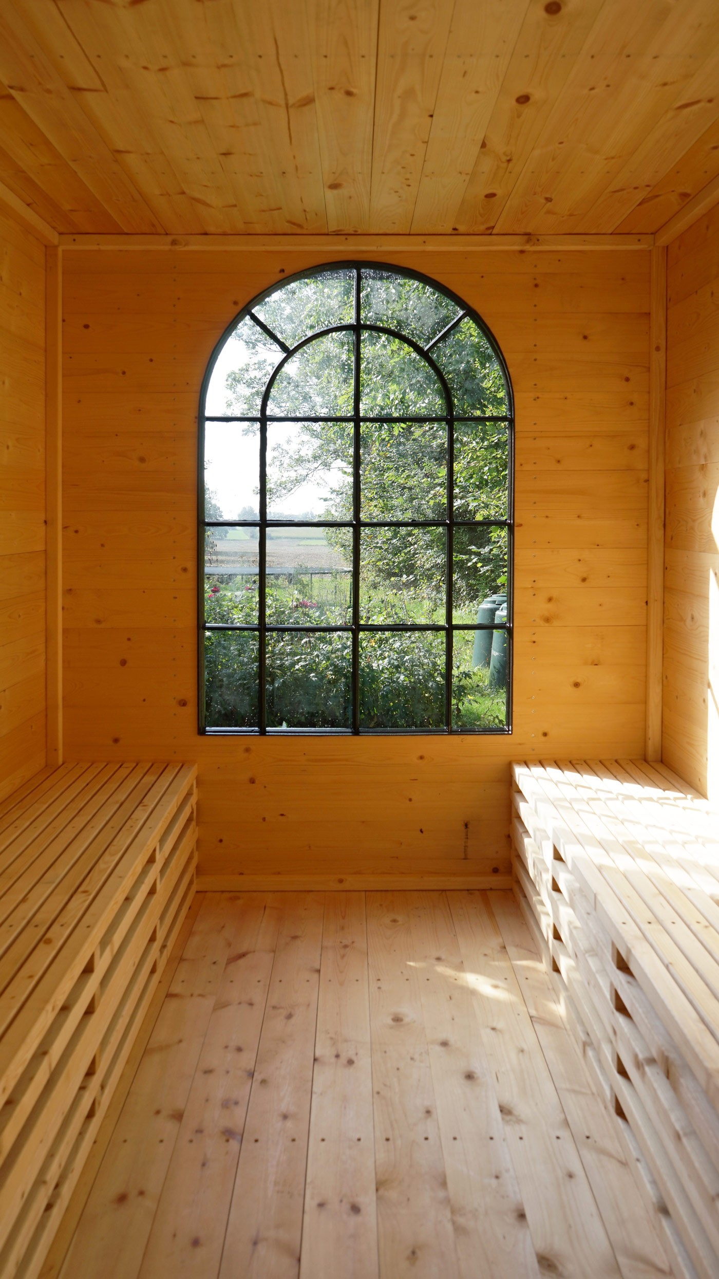Interior of Bakkely Sauna and Guest House with timber benches and arched window overlooking garden designed by Asger Risborg 
