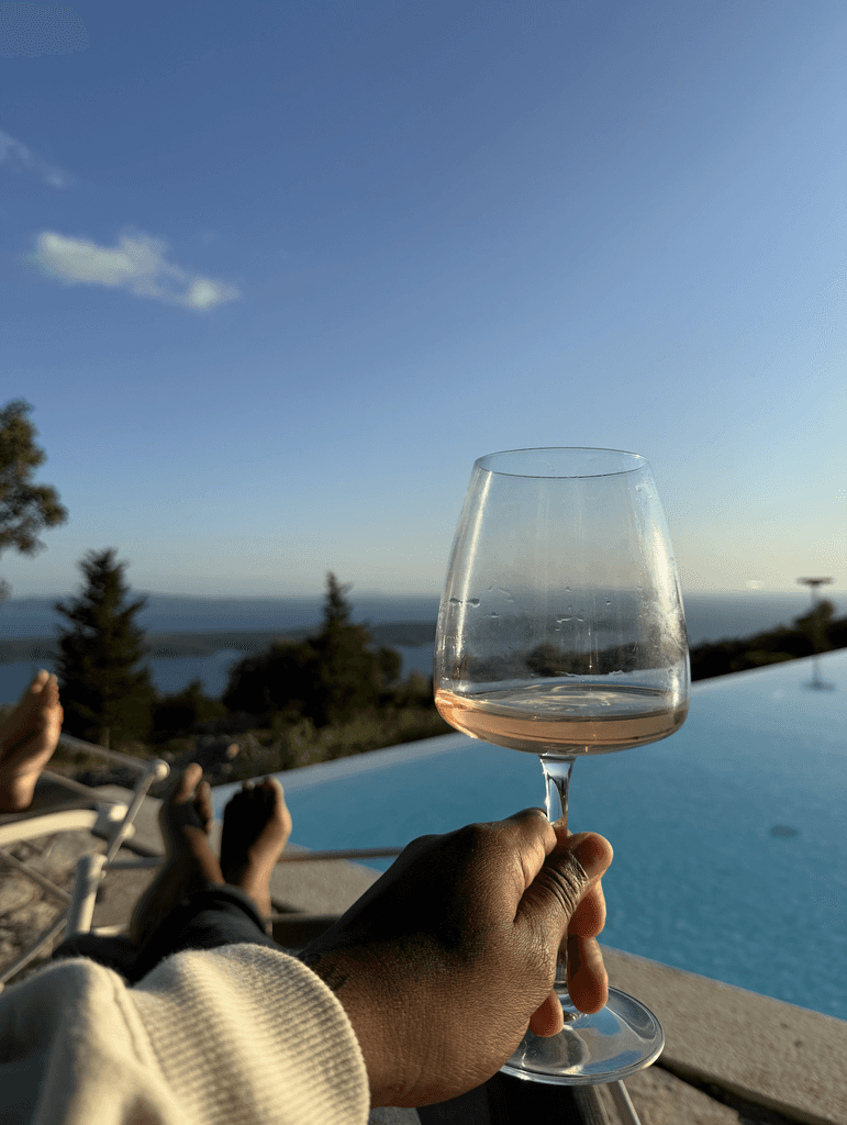 Ashleigh Warren holding a glass of wine, with a view of a pool and scenic landscape in the background.
