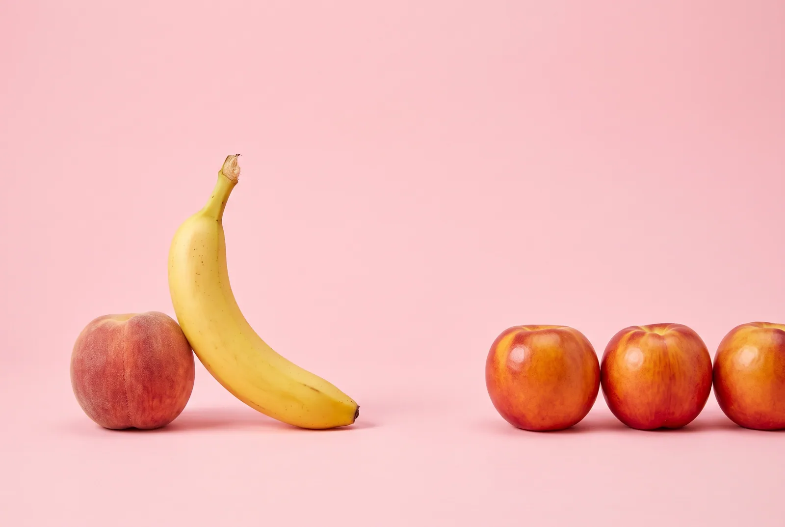Two peaches on a pink backdrop, one turned away toward a glossy plum, a playful image of a husband looking at women online