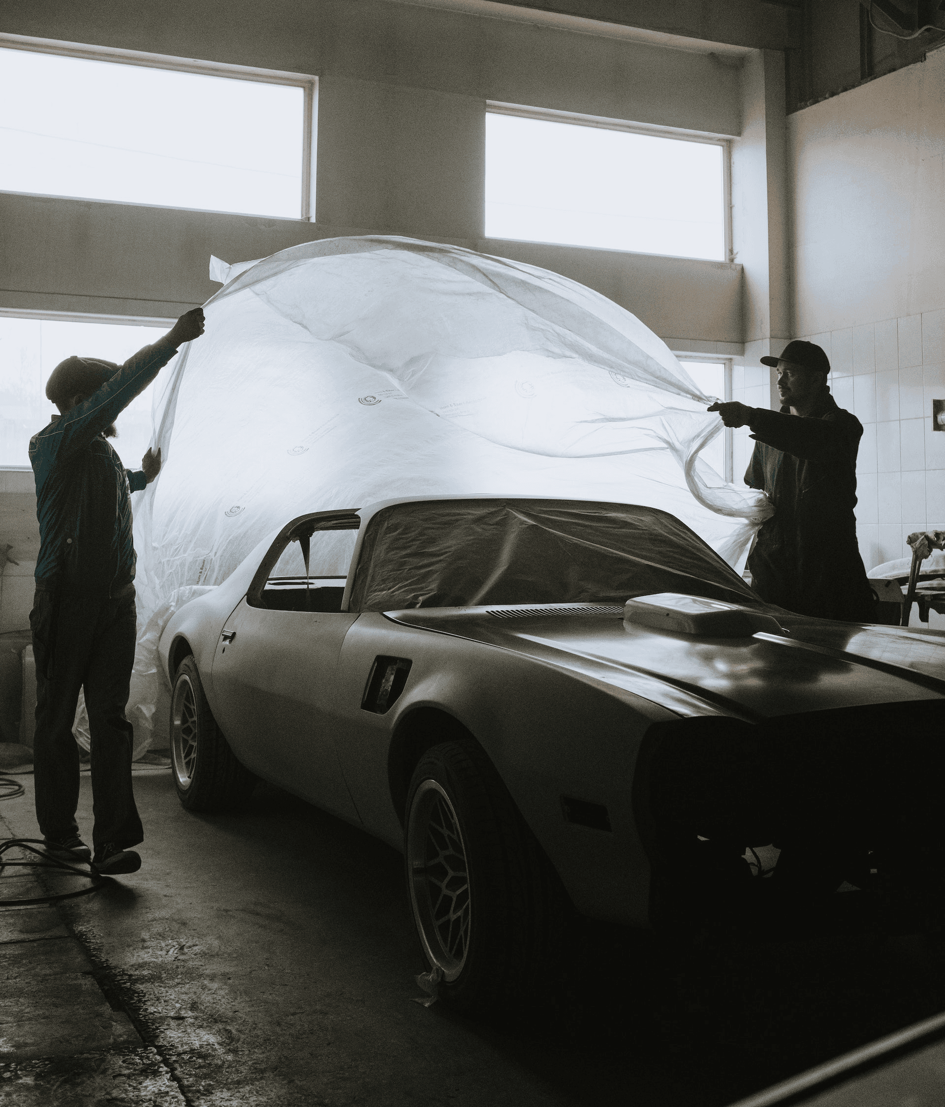 Two workers removing car's protection cover inside garage