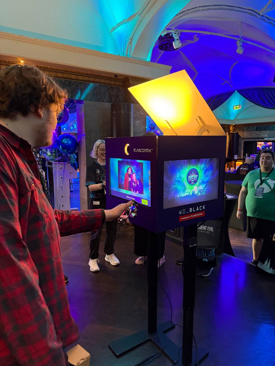 Ein Nutzer bedient das Touchdisplay der SnapCube® Fotobox CUBE. Der zusätzliche Screen zeigt ein Brandvideo von Sandisk. Die Fotobox dient als Fotoaktivierung auf der Gamescom in Köln.