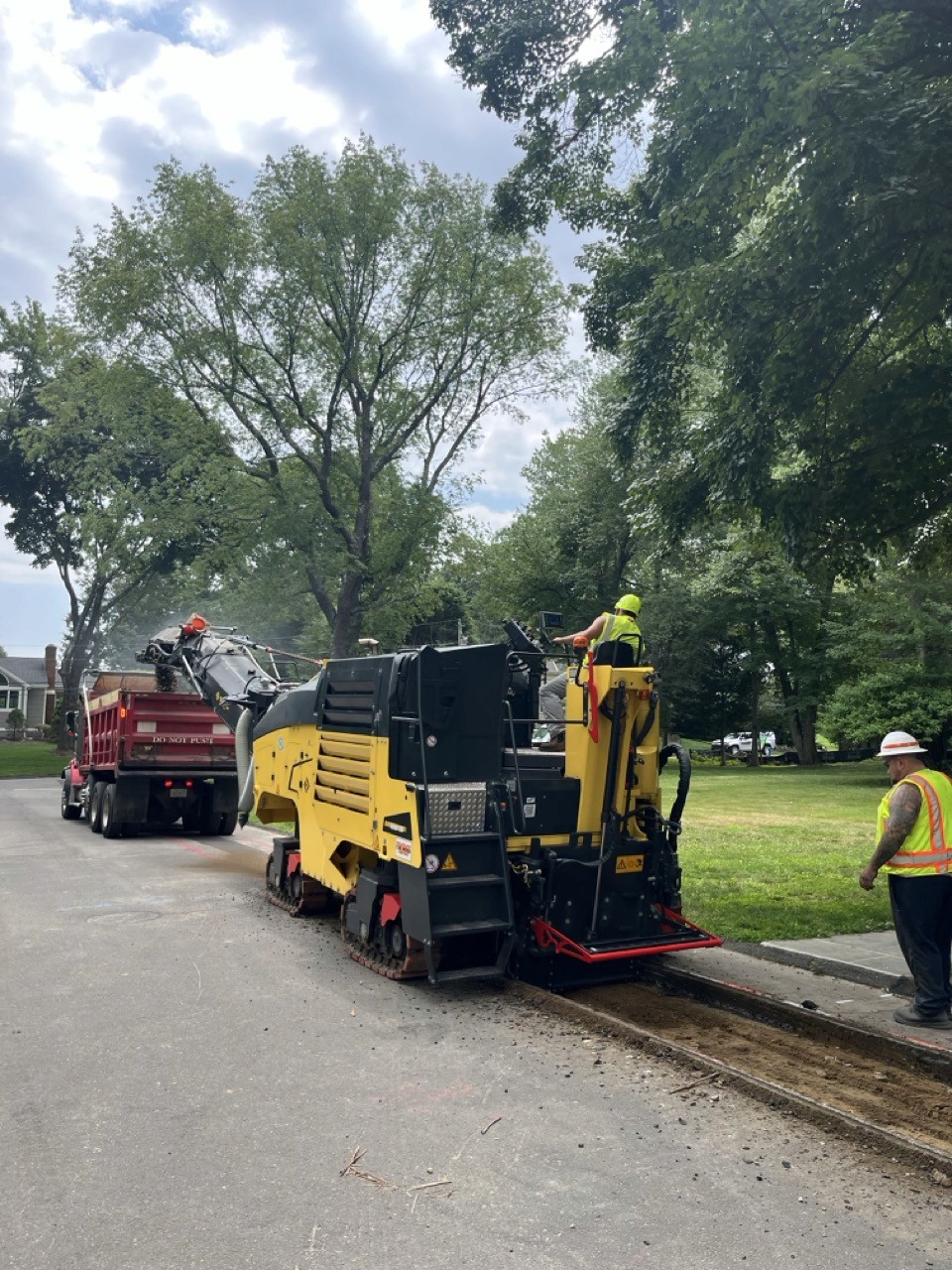 Cold planer loading millings into a truck on a tree-lined street, A&M Construction jobsite
