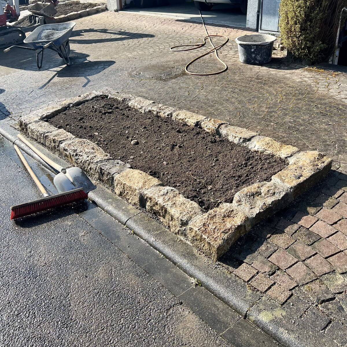 Detail einer Garten-Neuanlage in Weingarten: Mit Natursteinen eingefasstes Pflanzbeet, integriert in eine gepflasterte Fläche.