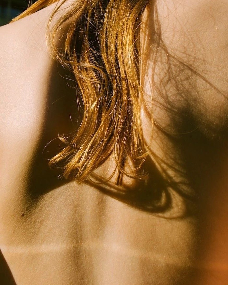 braided woman taking photo beside yellow painted wall