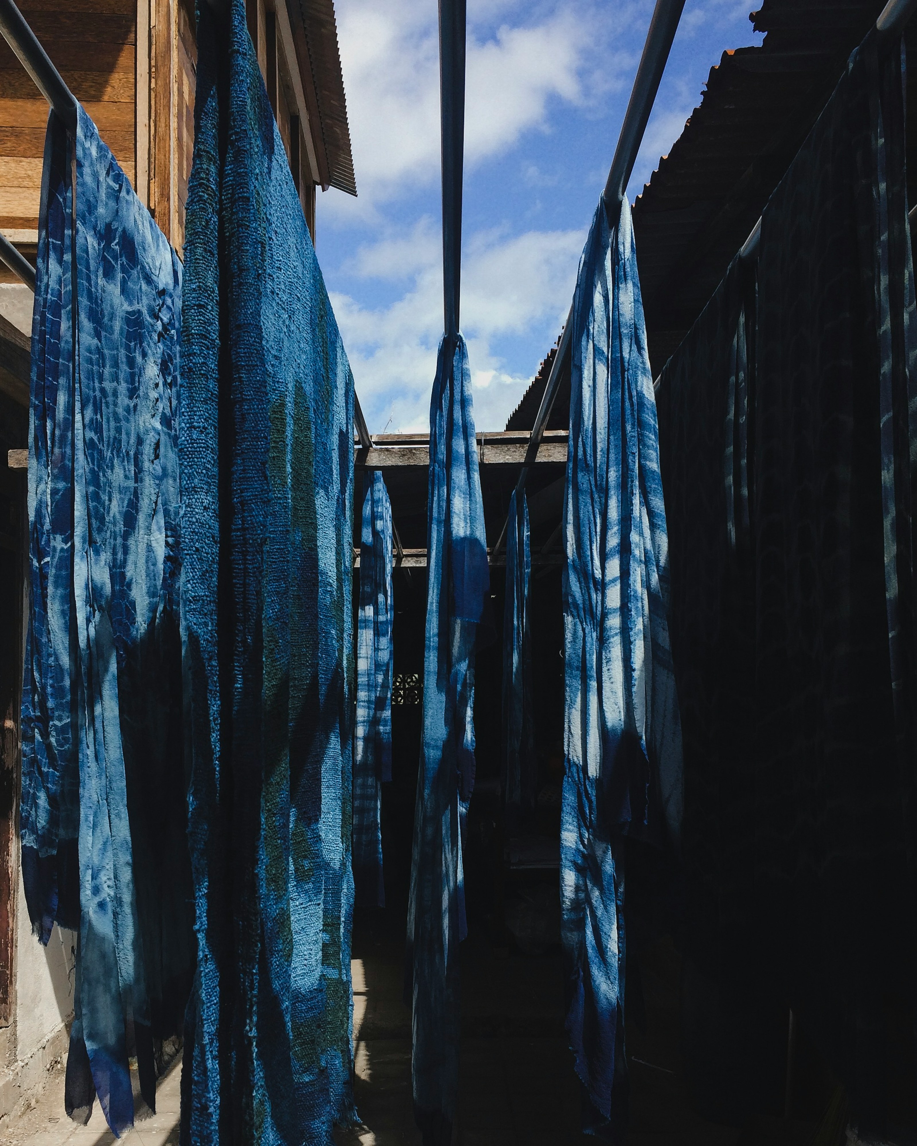 Lengths of indigo-dyed cloth drying between wooden buildings