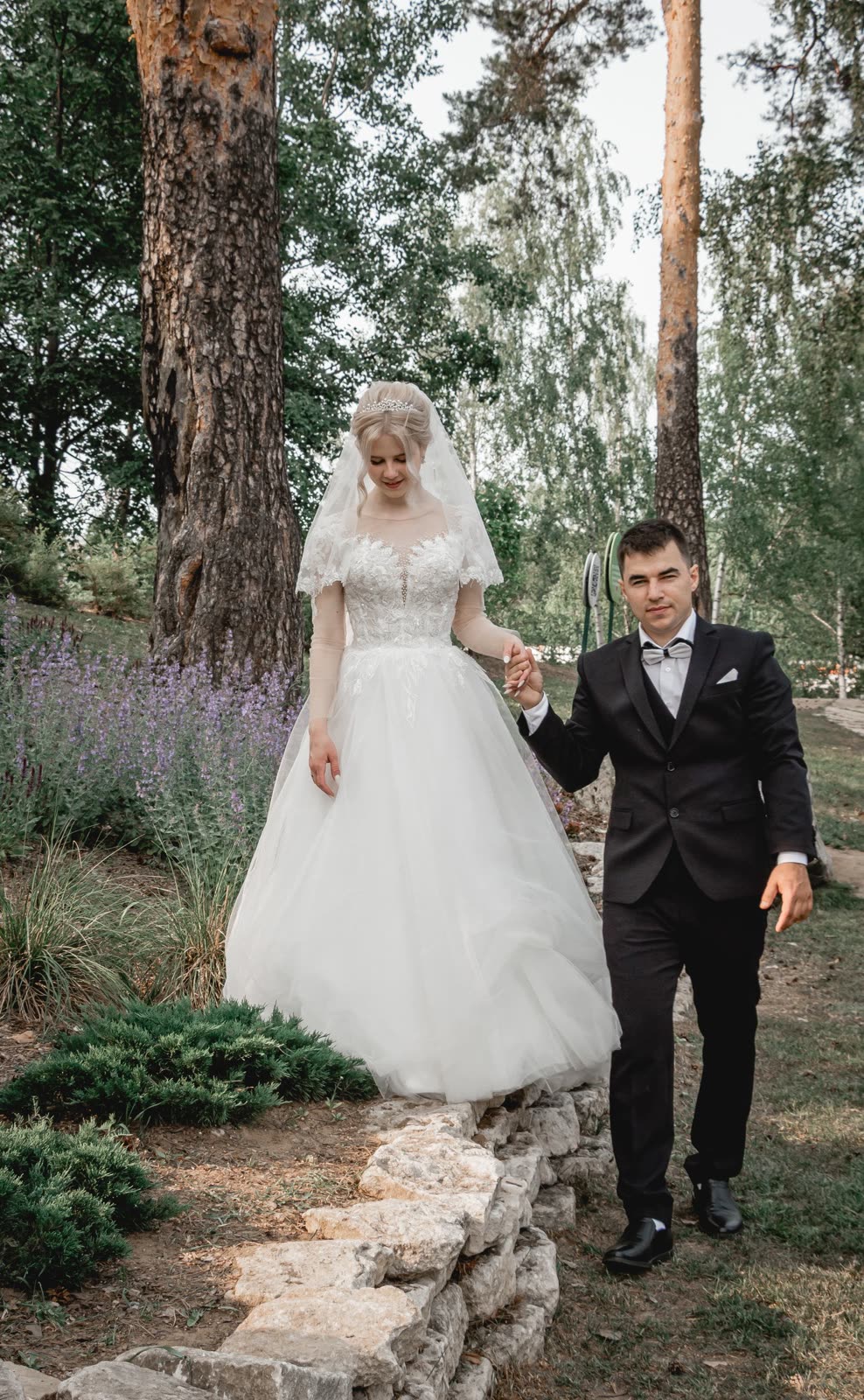 Bride and groom standing among lavender plants with tall pines behind them