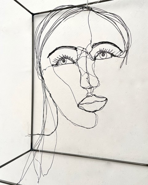 Sculpture en fil de fer représentant le visage d'une femme dans un cadre en fil de fer, vue détaillée de côté avec son ombre projeté sur le mur
