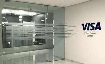 Modern office interior featuring a glass wall and a prominent Visa logo sign on the white wall. 