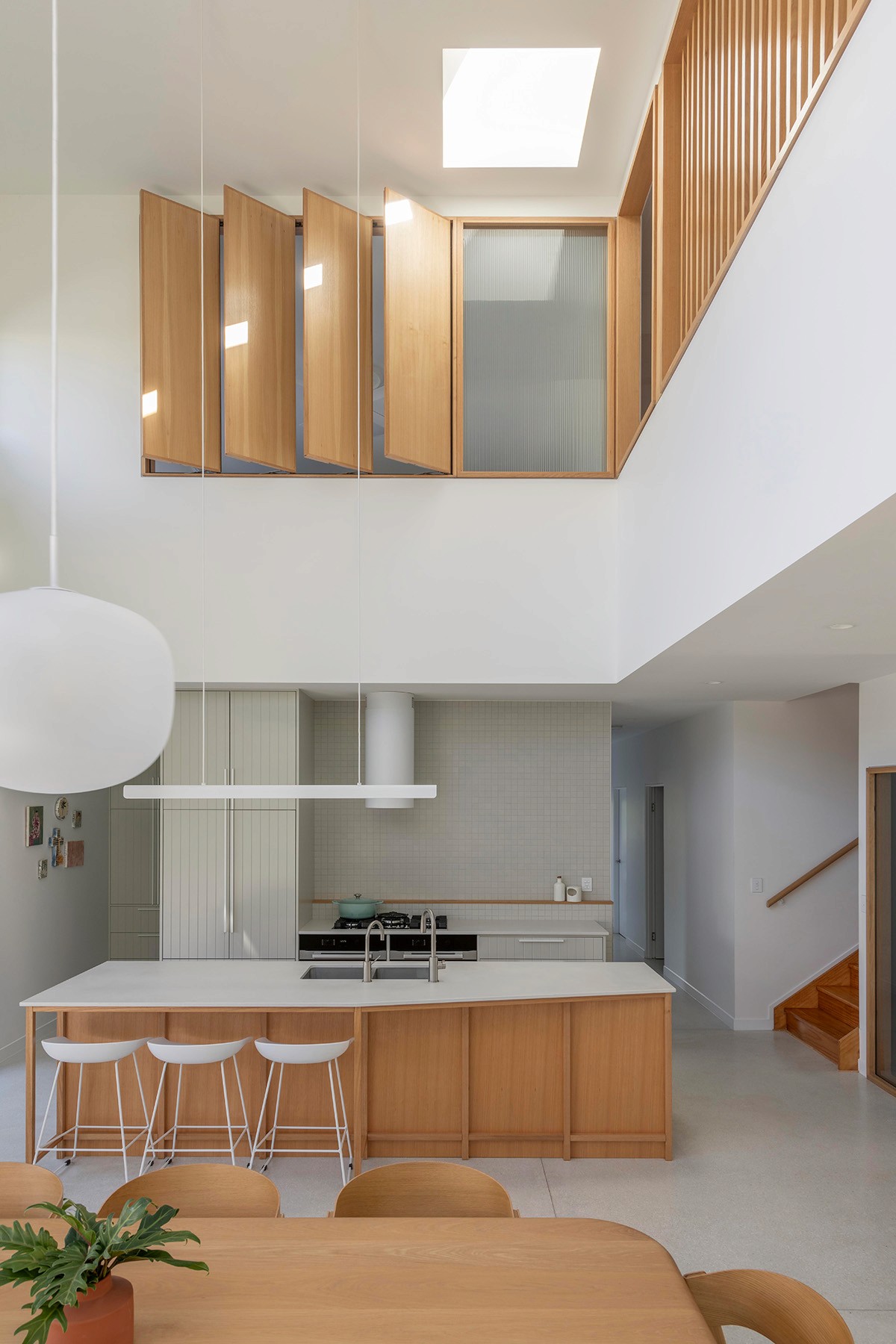 Double-height kitchen with timber joinery, skylight, and sculptural stair balustrade above.