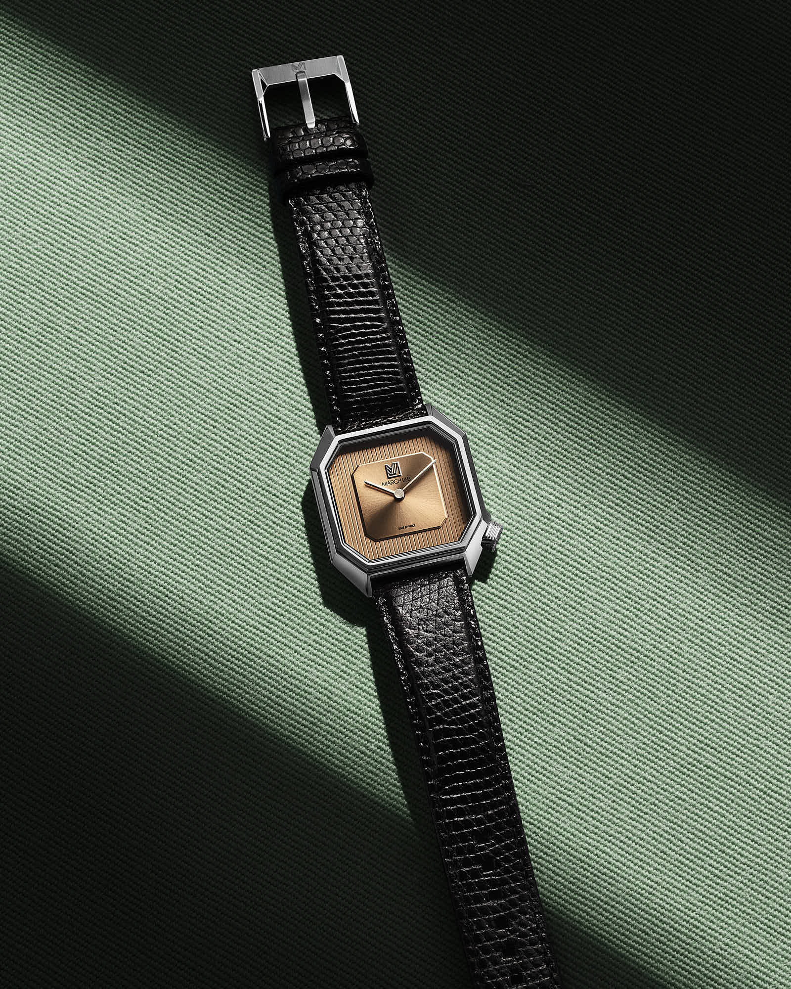Luxury wristwatch with black leather strap and octagonal dial on a green background