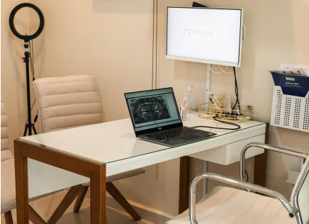 Consultório moderno da Nahser Odontologia no Rio de Janeiro: ambiente clean com mesa de atendimento, monitor e laptop exibindo radiografia digital, equipado para atendimento odontológico.