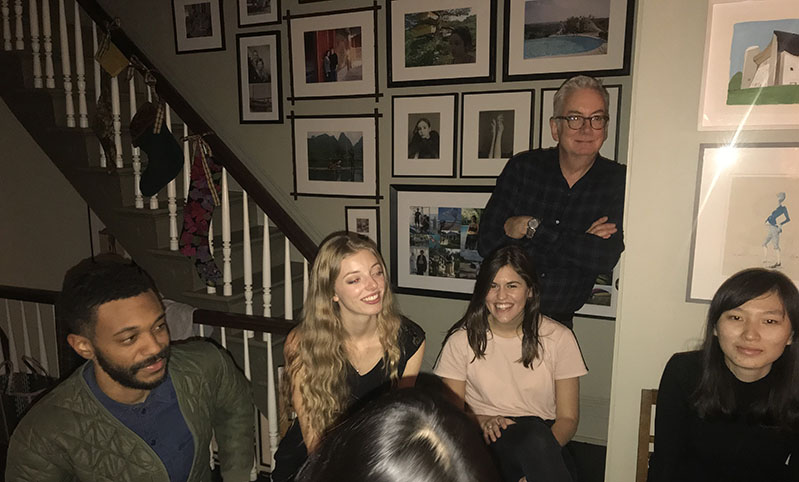 A photo with a group of people sitting near a staircase and a wall filled with family photos.