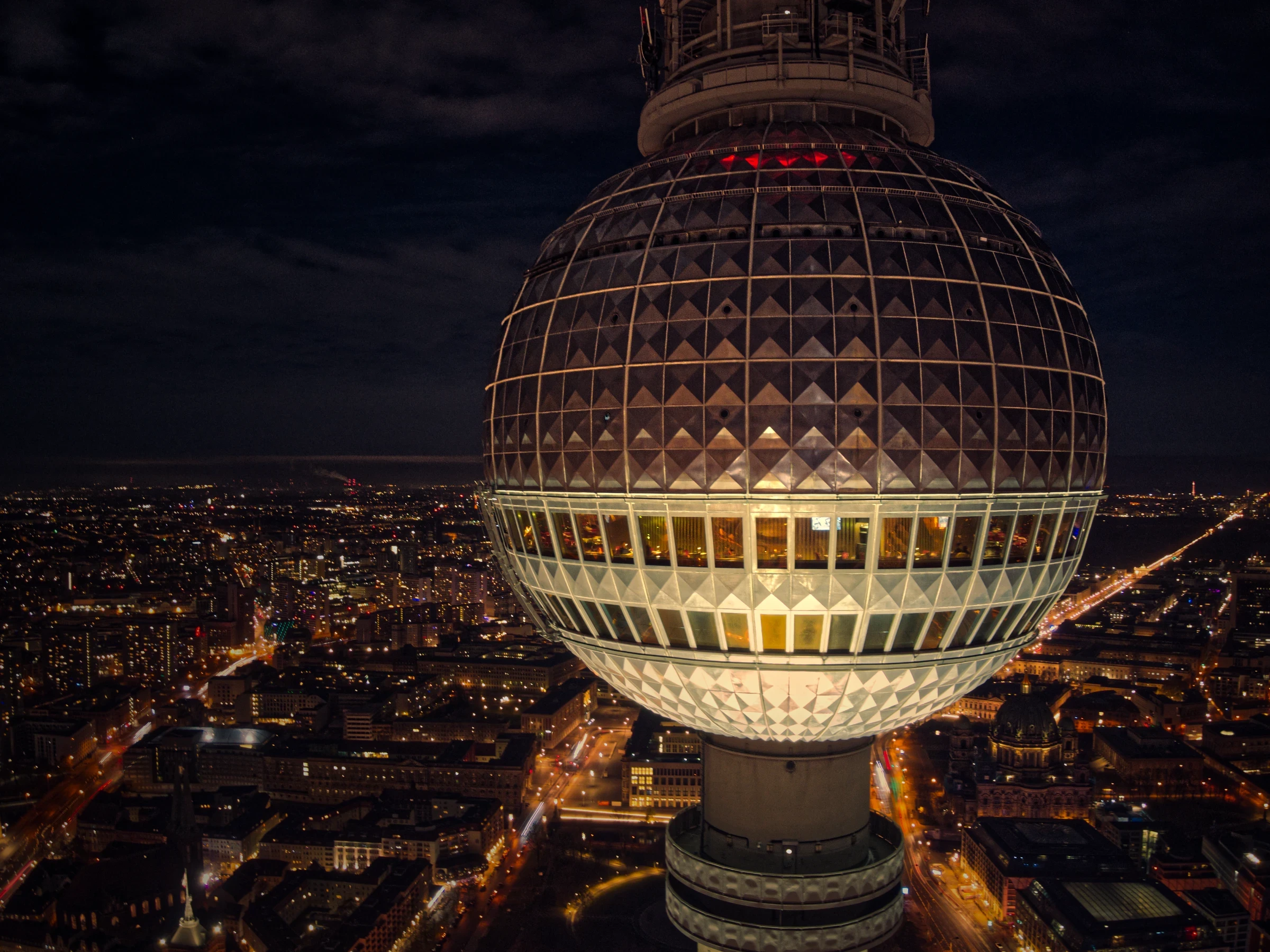 Berliner Fernsehturm bei Nacht aus nächster Nähe fotografiert. Die beleuchtete Kugel mit dem Restaurant Sphere dominiert die Skyline von Berlin.