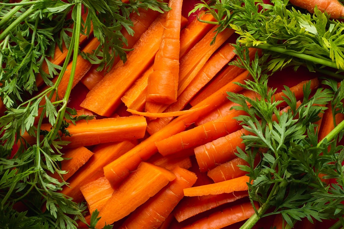 A pile of fresh carrots and parsley on a table, examples of fiber-rich vegetables to offer picky eaters