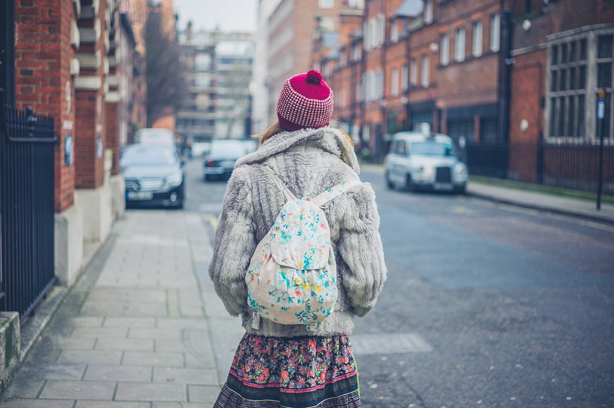 The back of a woman on a cold street in London. She is wearing a wooly hat and fleece, carrying a backpack