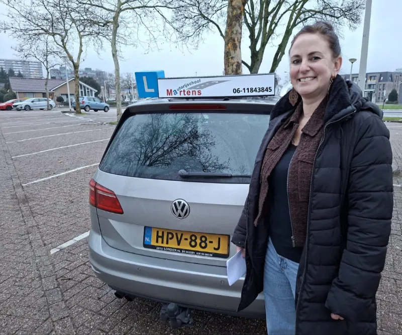 Geslaagde leerling die de duim omhoog steekt voor de lesauto van Rijschool Martens.