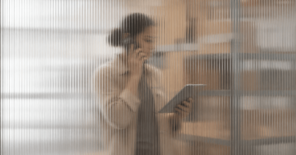 Operations associate verifying an order by phone in a warehouse, seen through vertical fluted glass