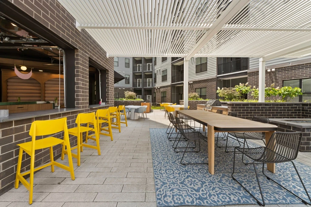 Patio at the park featuring a grill and garage windows, surrounded by greenery and outdoor seating.