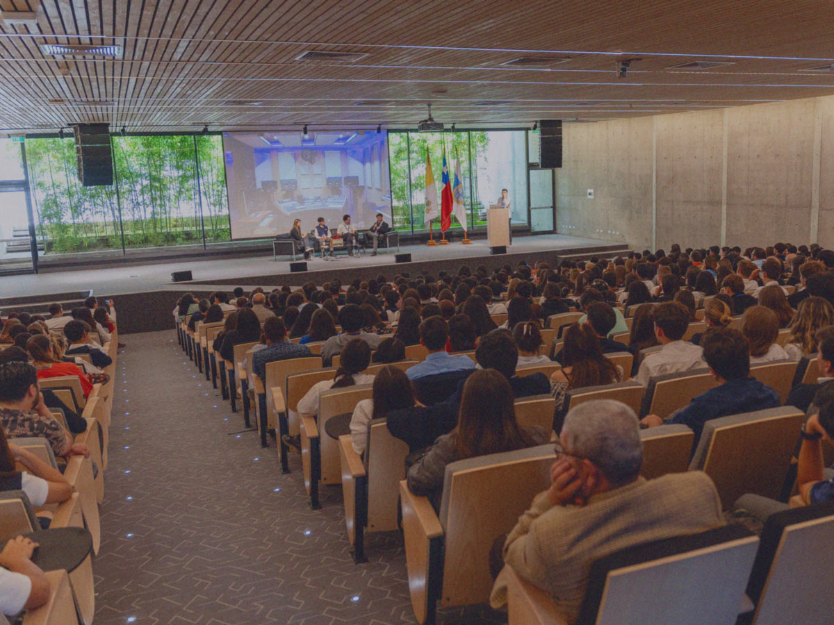 Estudiantes y expositores comparten en un escenario mientras decenas de estudiantes los observan en un auditorio lleno en un evento de IdeaPaís.