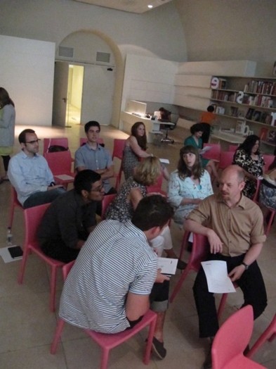 A photo of a group of people sitting on pink chairs, talking and comparing lecture notes.