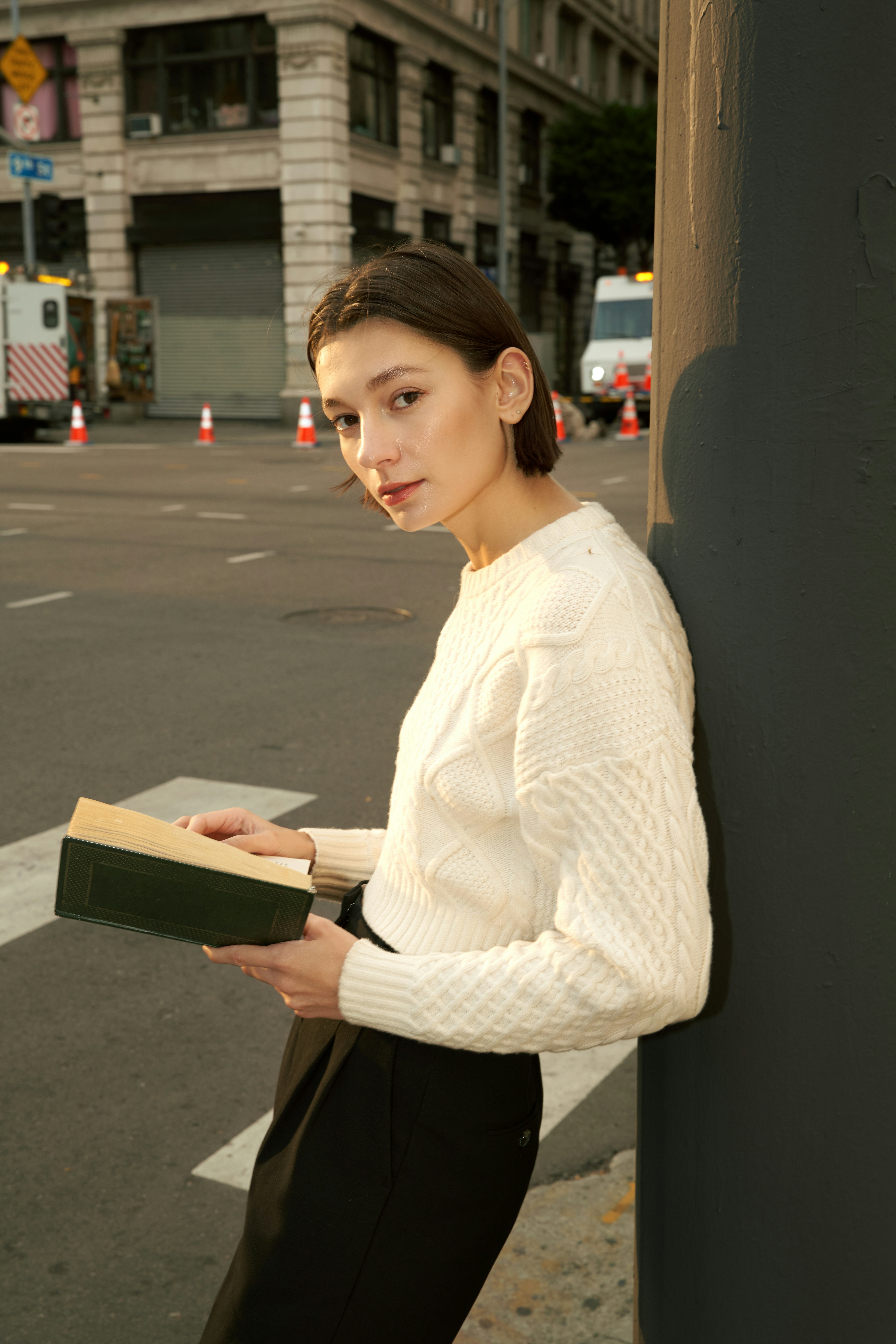 woman standing against a pole with an open book in her hands