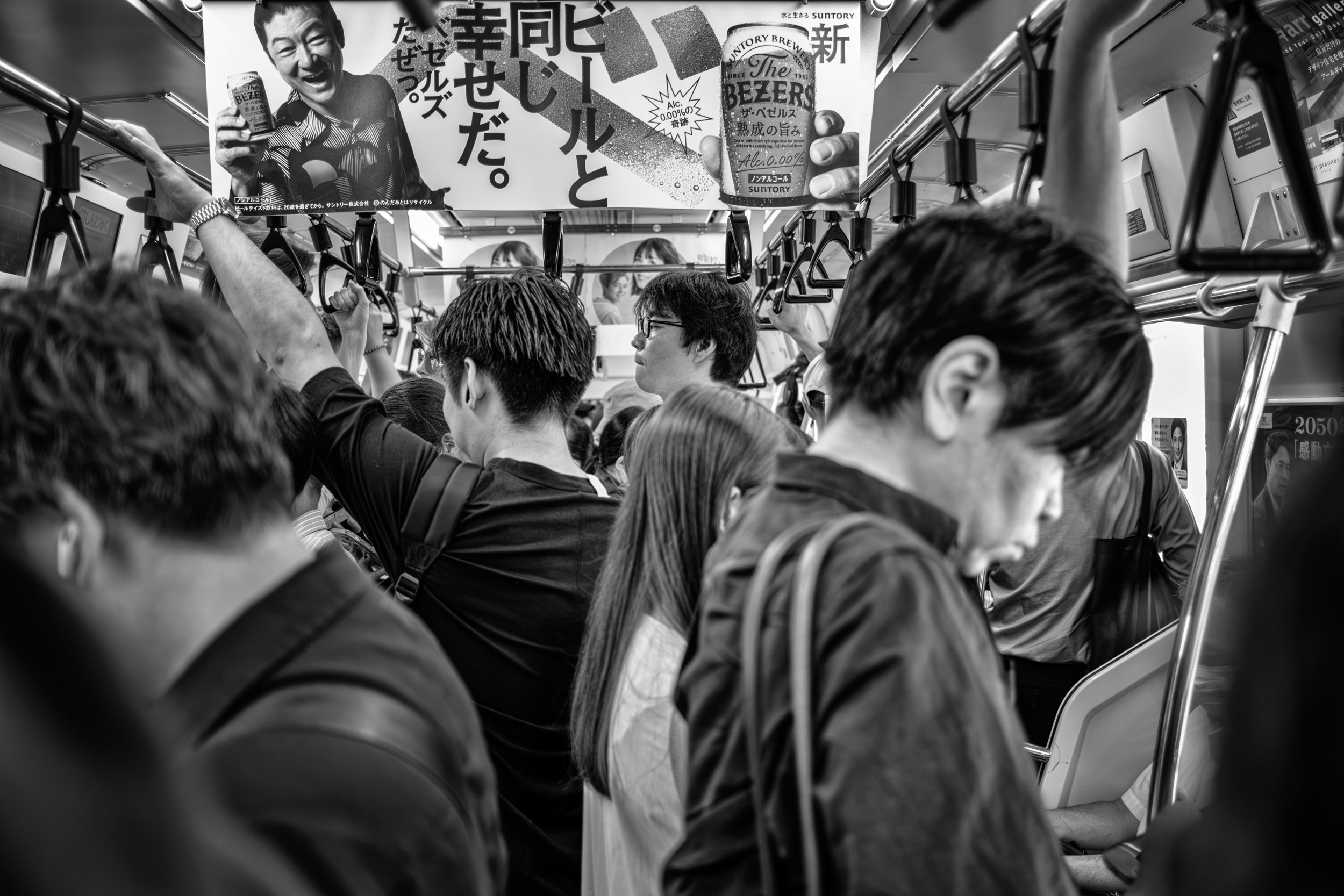 Black and white close-up image of a packed train interior with commuters standing tightly together.
