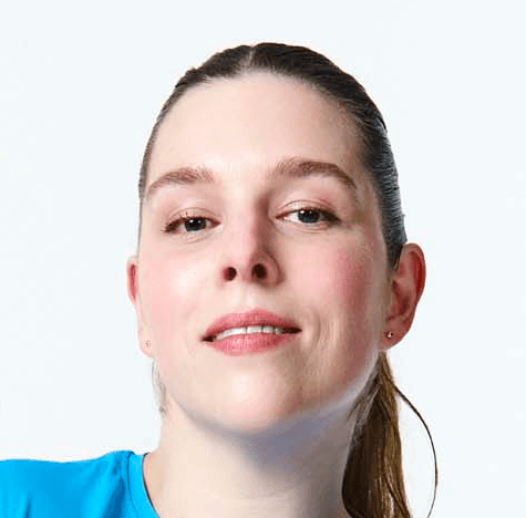 A person with short, dark hair smiles at the camera, wearing a black shirt against a backdrop.