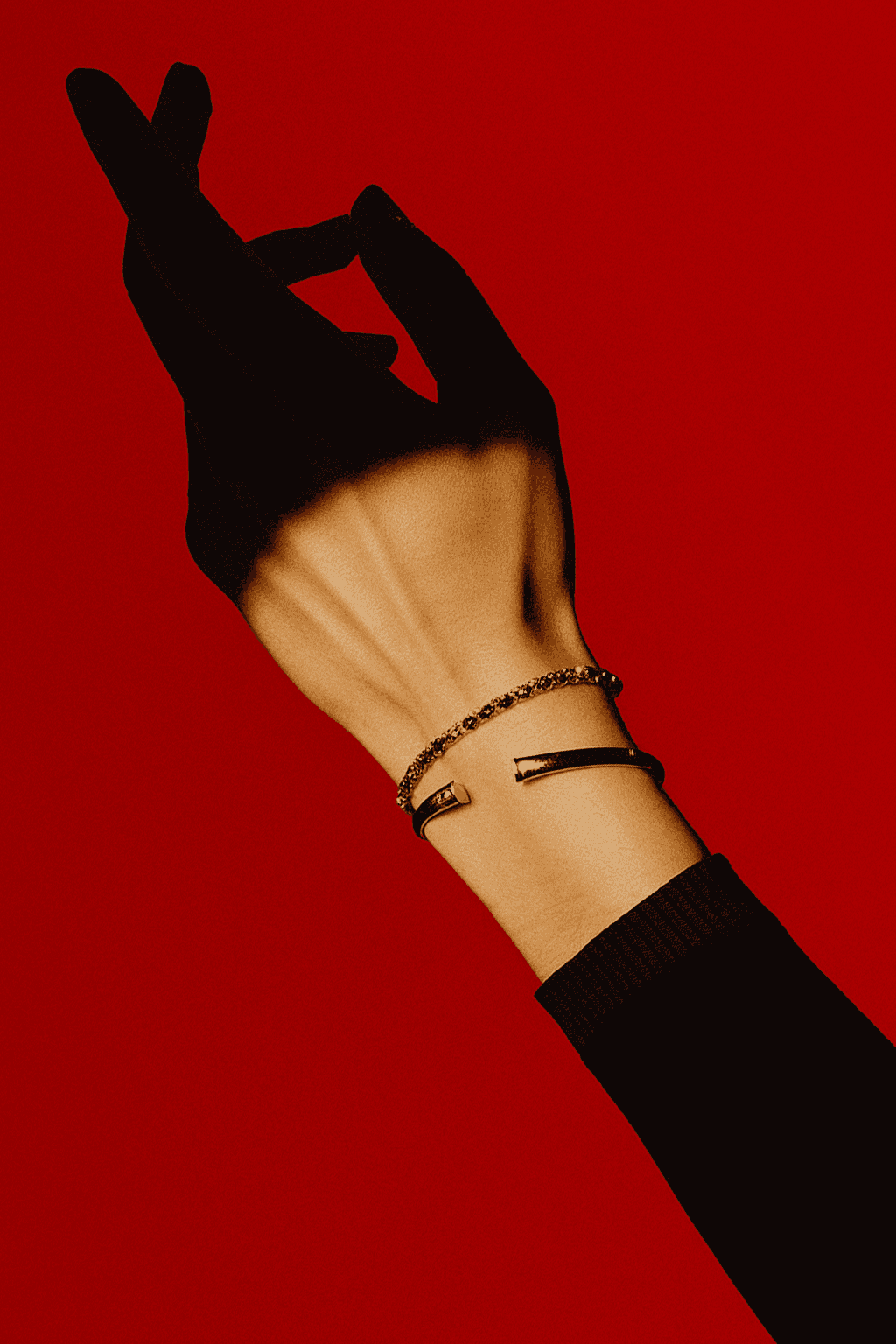 Elegant hand against a red background wearing two gold bracelets, one sleek and minimal, the other a delicate chain.