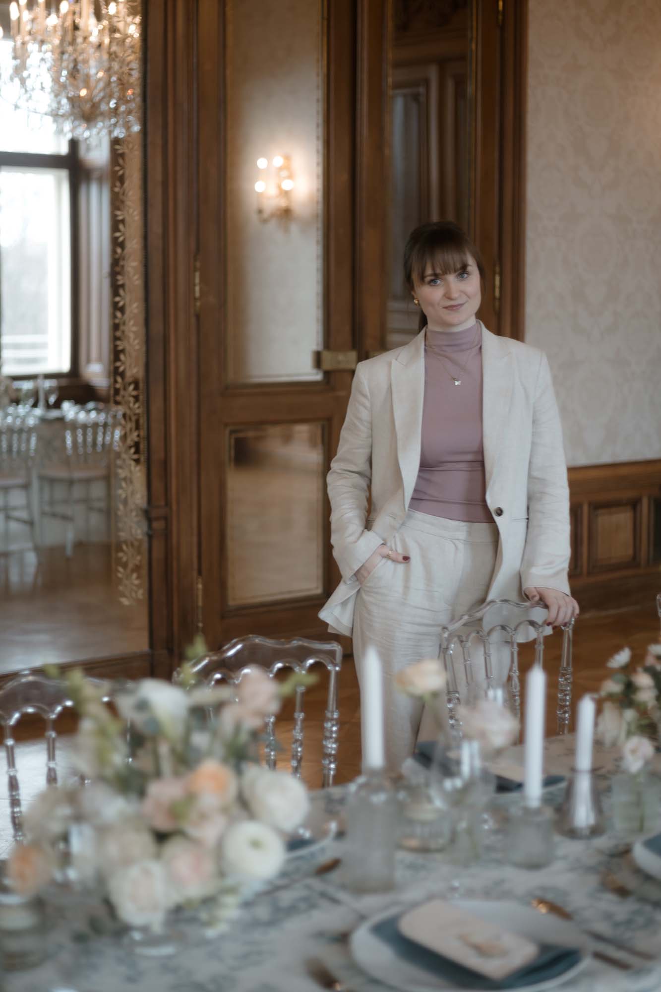 Hochzeitsplanerin Emily steht in einem Wiener Ballsaal hinter einem Table Setting einer Hochzeit - romantisch.