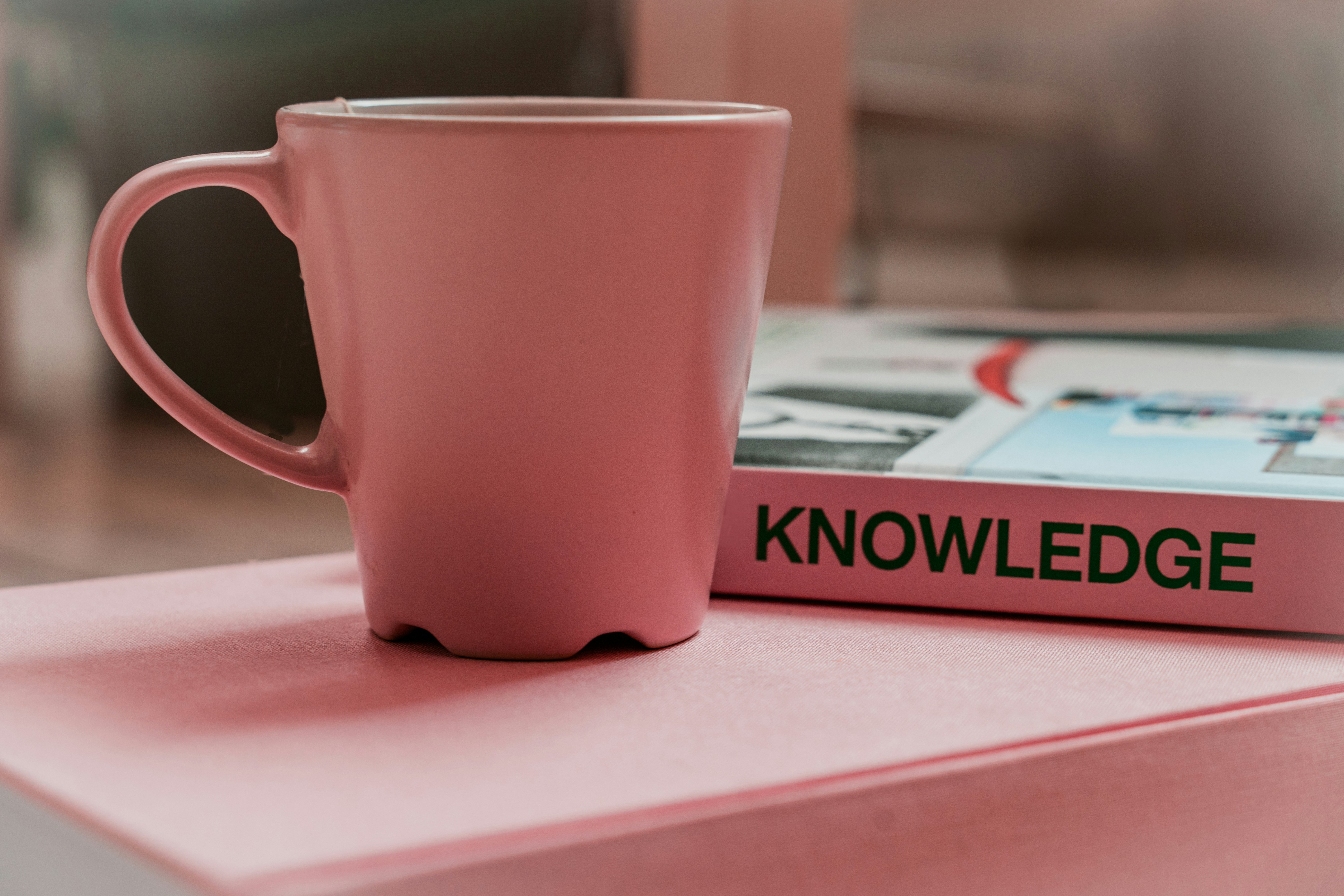 image of pink coffee cup and a pink book with knowledge written on the spine. photo by Gabriella Clare Marino
