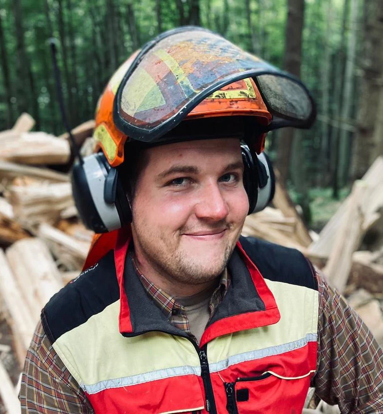 A forester poses with a chainsaw in the woods.