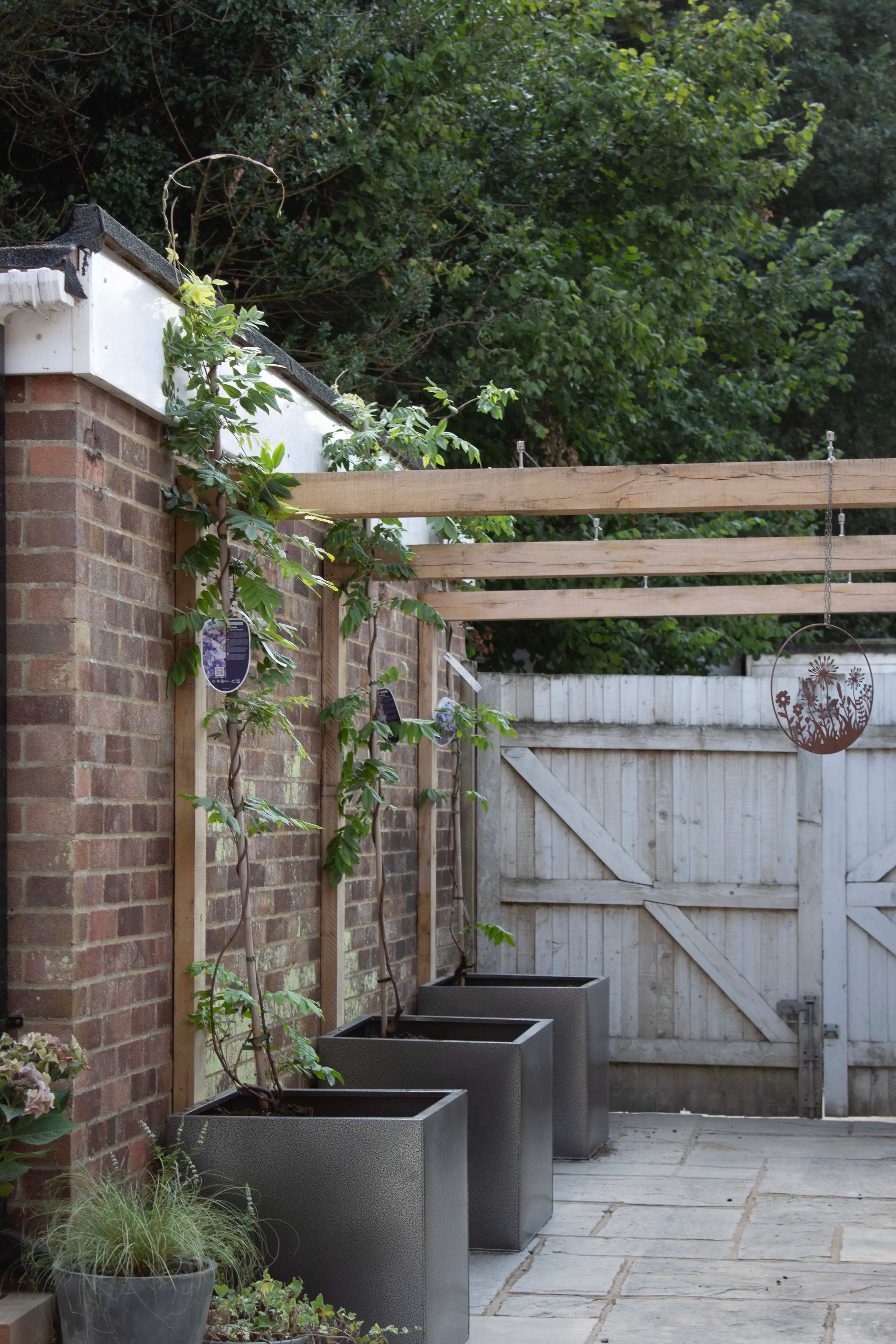 A garden gate made of wood, surrounded by plants and potted greenery, leading to a fenced area.