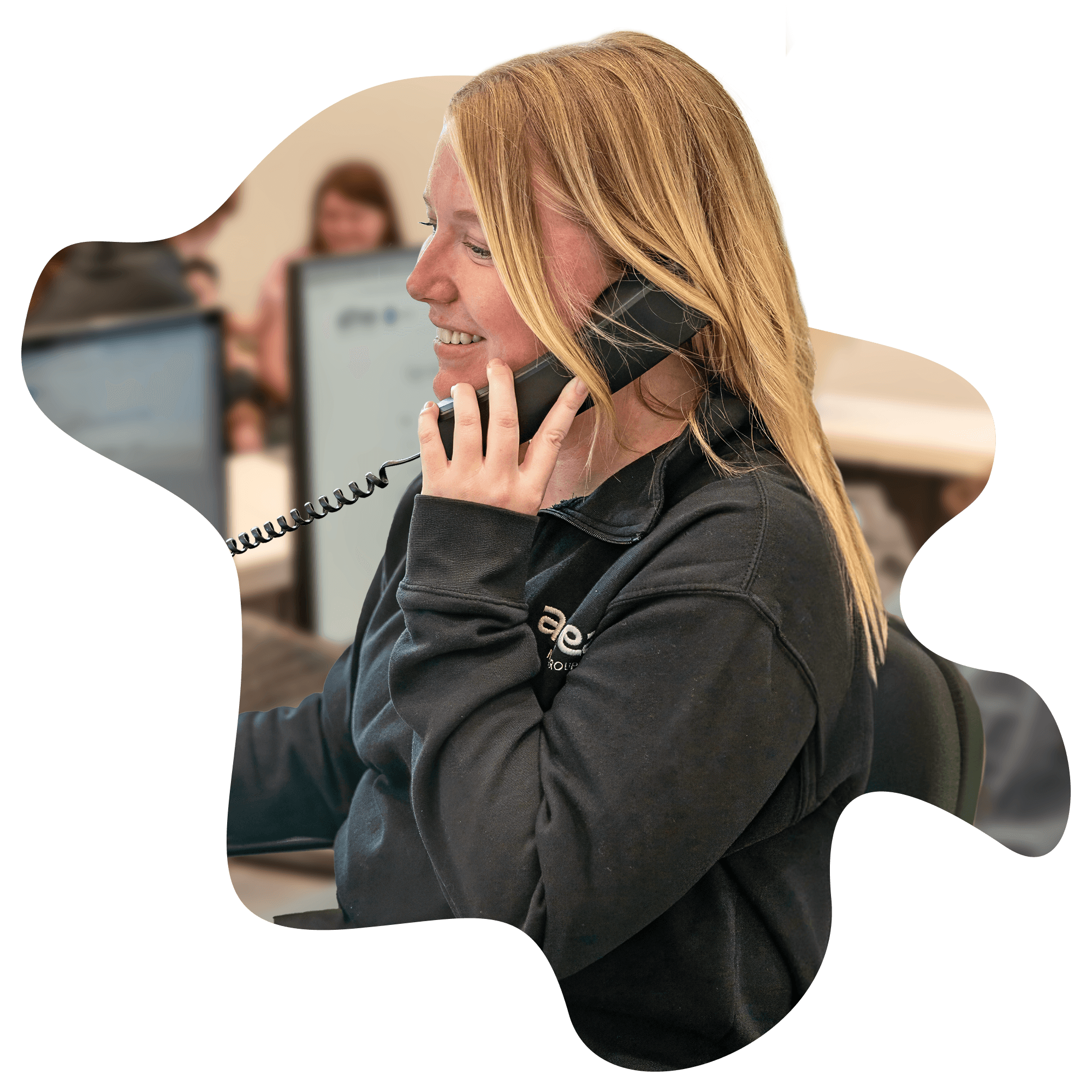 A woman talking on the phone while working at a computer in an office environment.