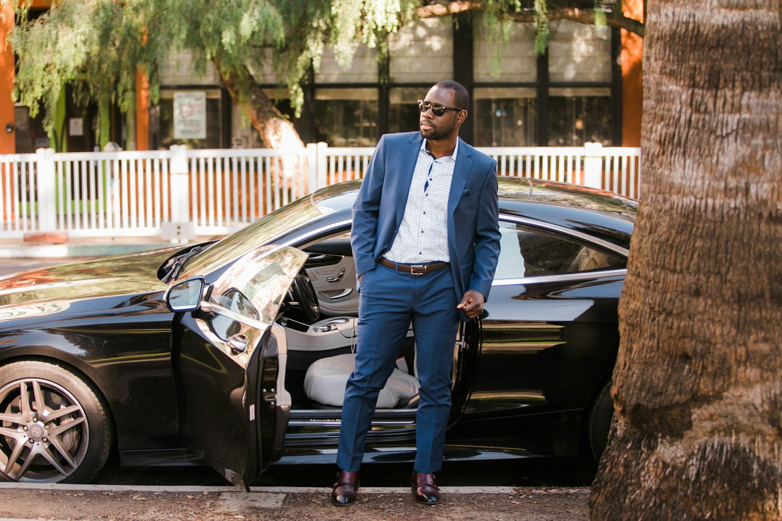 Chauffeur in a suit standing beside a black luxury sedan with the door open