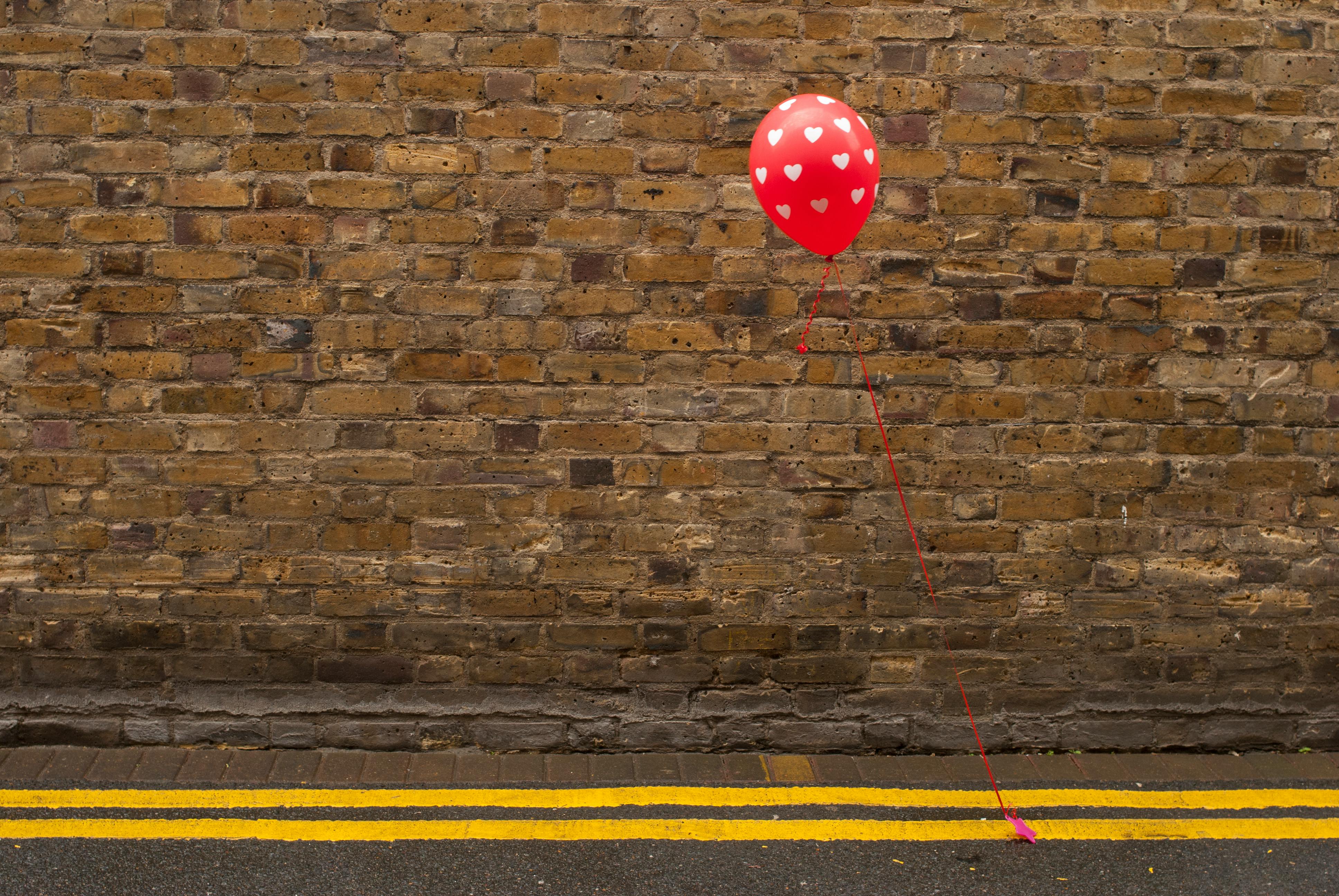 Red heart balloon tied against brick wall