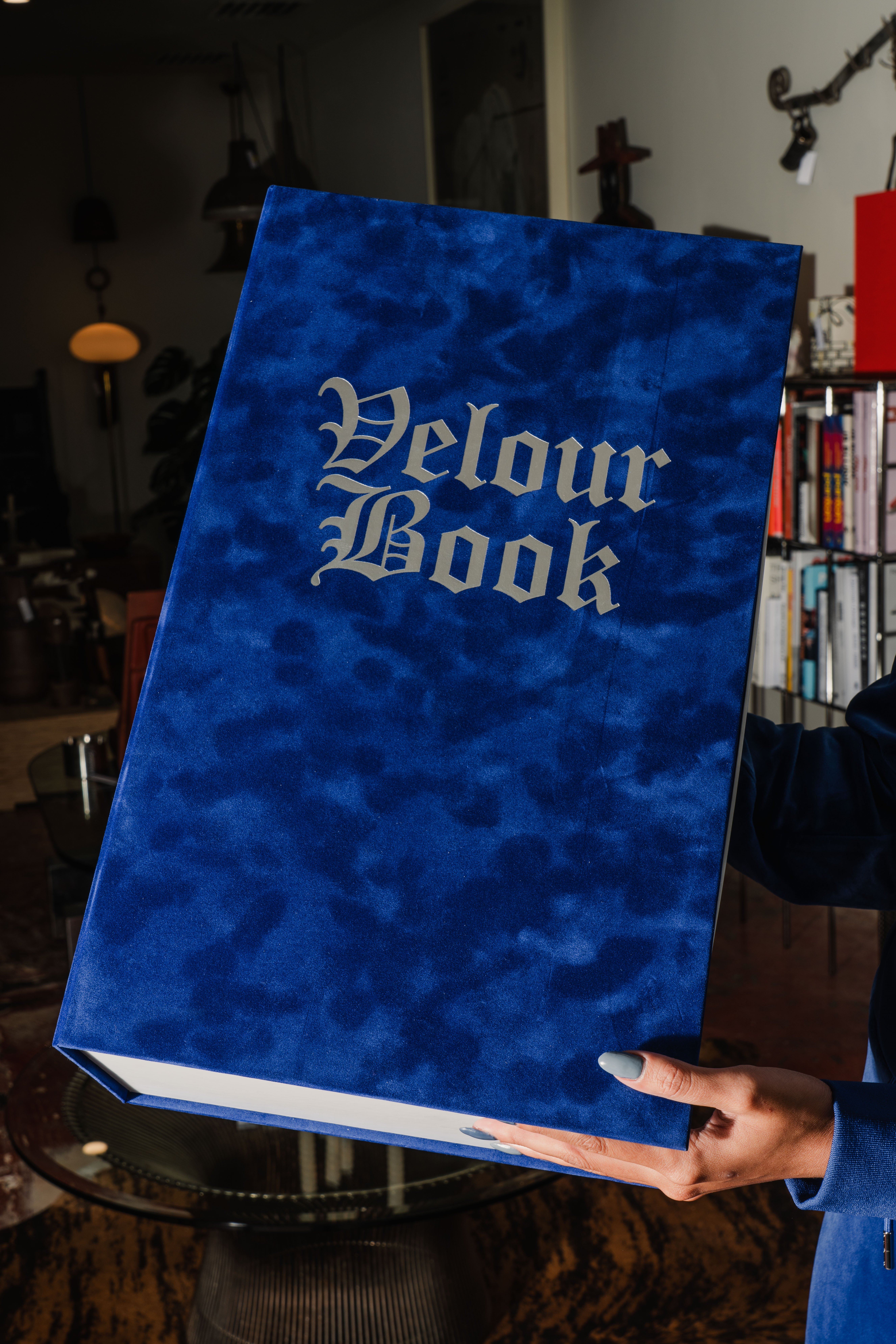 Large blue velvet box being held up in a room that has the words "Velour Book" in silver on the upper top of the box.