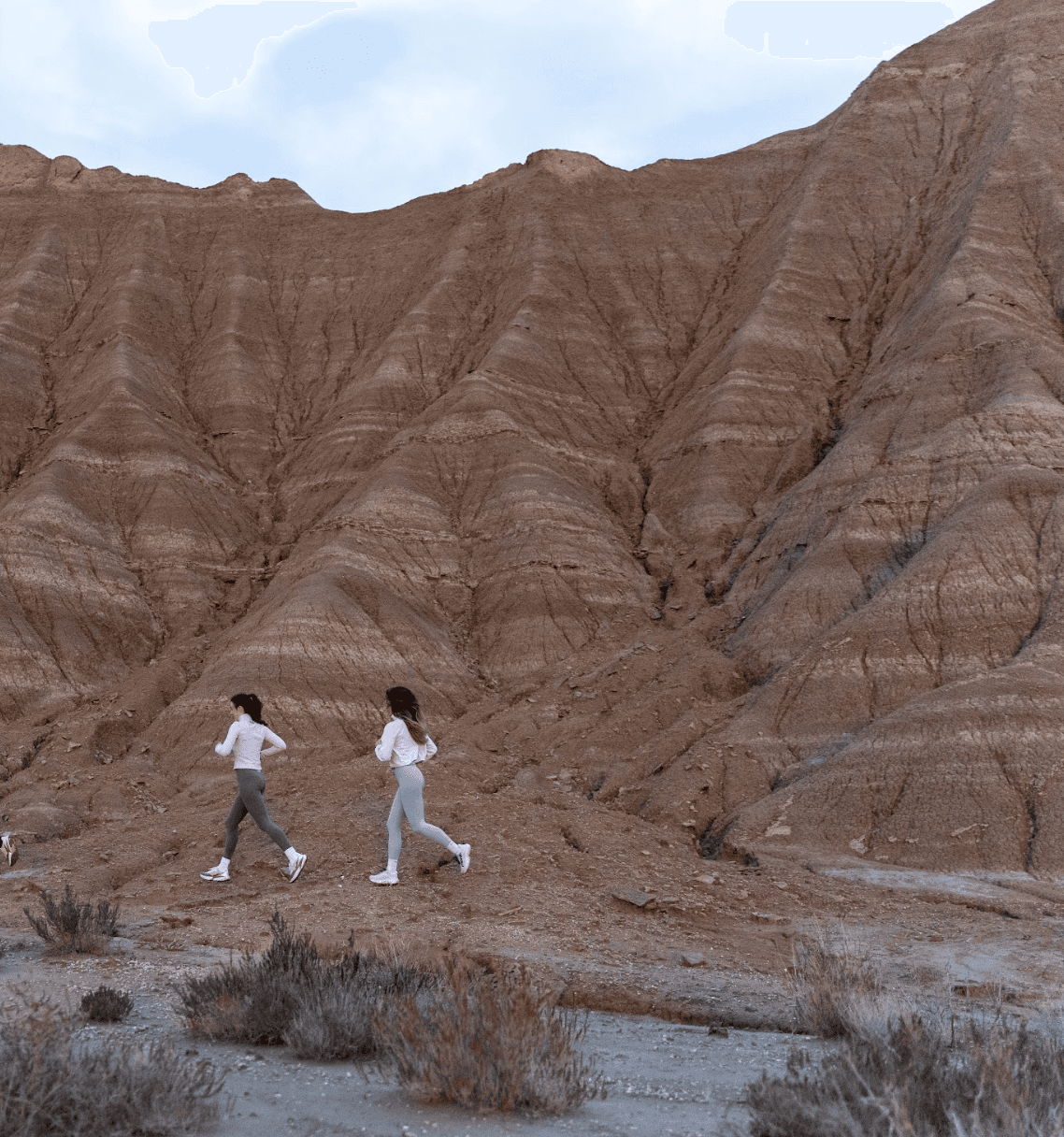 Man wearing olive green and orange sneakers with tall socks, standing on an urban street with a modern fence and skyscraper in the distance.