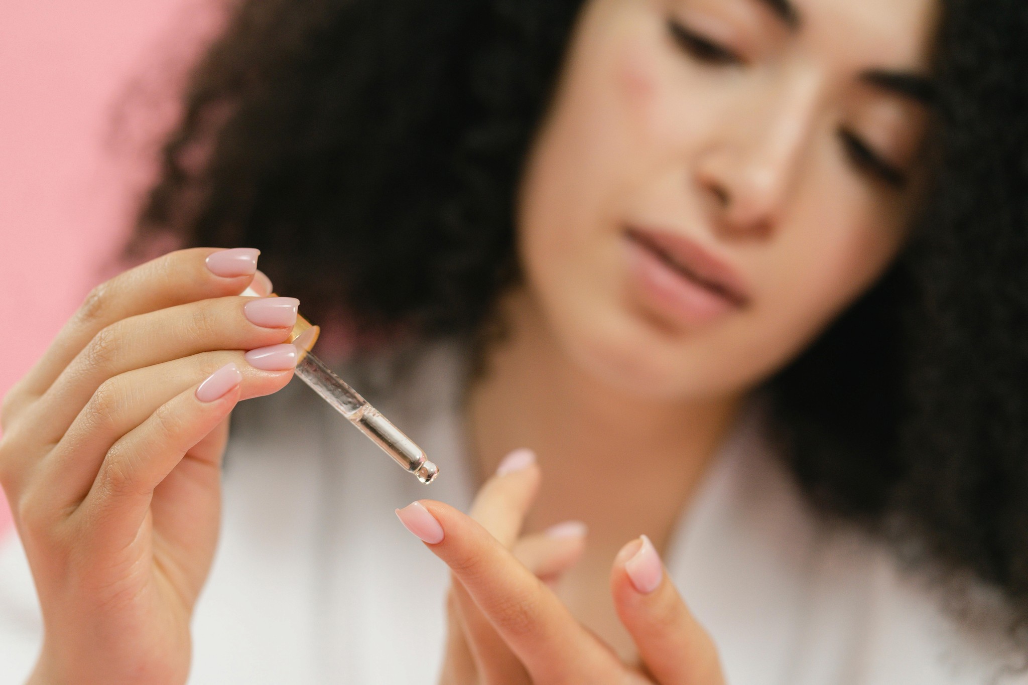 Woman applying cuticle oil with a dropper on manicured nails