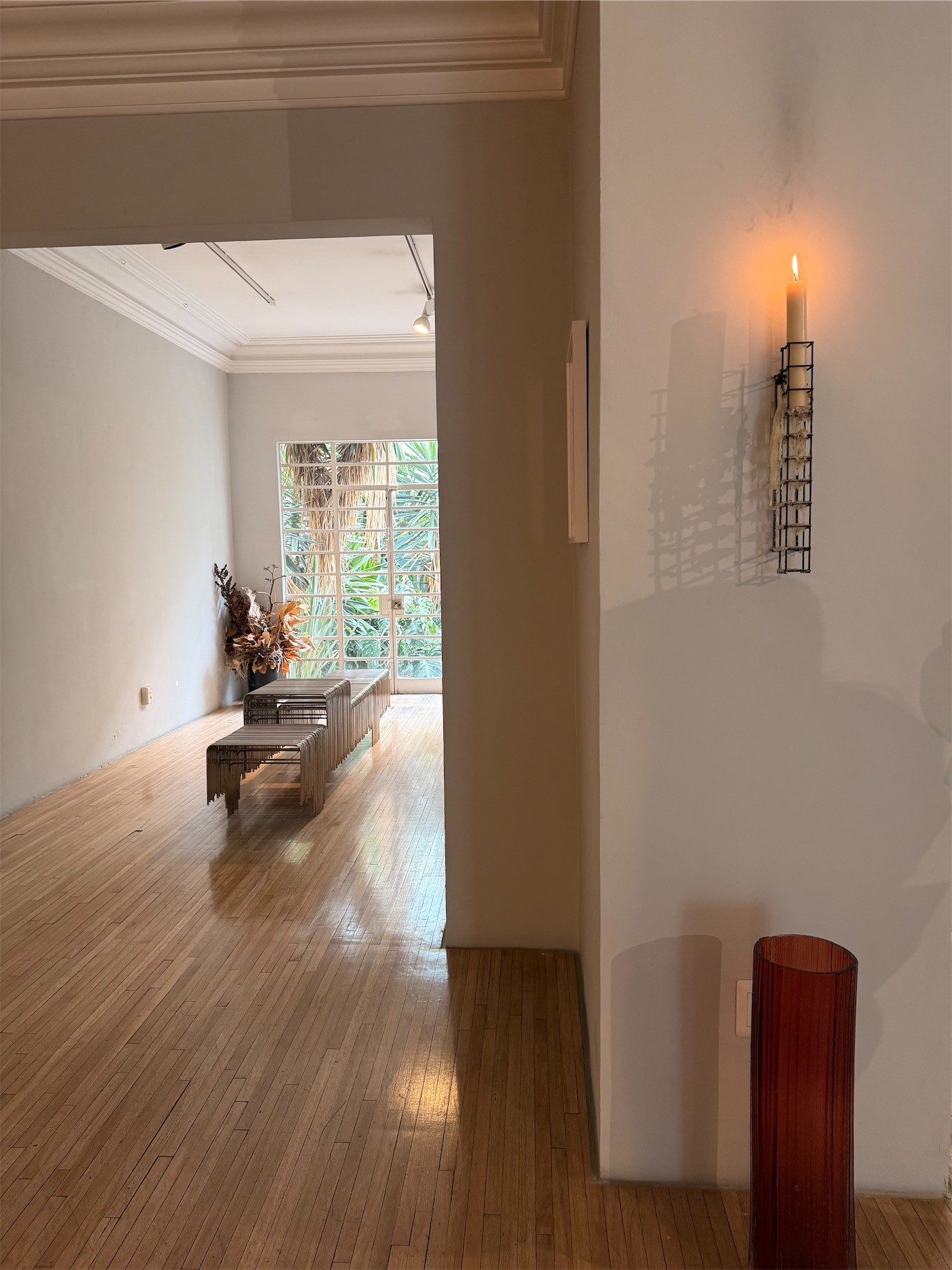 A white room with a candle sconce and a bench on a wooden floor
