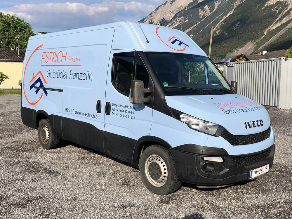 Ein hellblauer Lieferwagen der Firama Gebürder Franzelin Estrich parkt auf einer Einfahrt; an der Seite des Wagens befinden sich ein Logo und der Firmenname.
