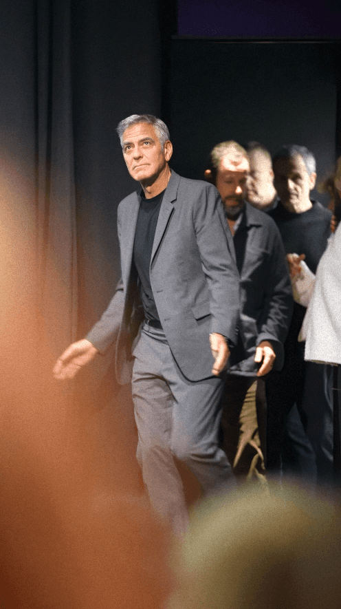 Bride sitting on ground against wall, groom standing nearby