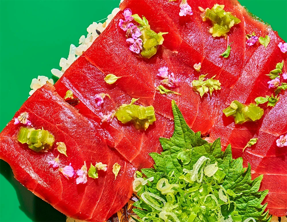 Tuna sushi with edible flowers and wasabi on a green surface