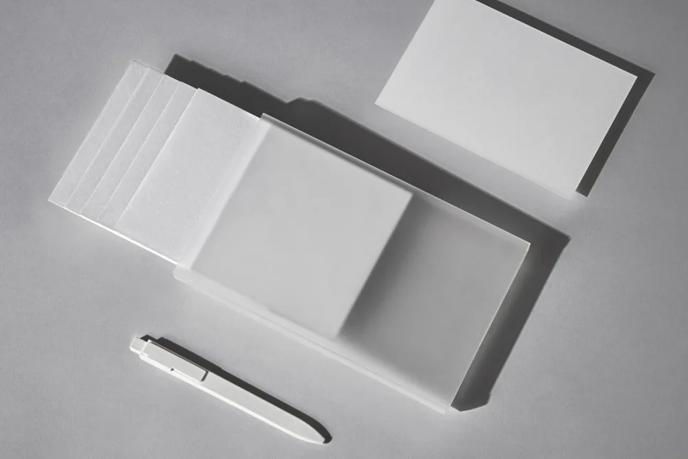 Identity stationery mockup featuring black cards with green text, a transparent case, and a pink invitation card. Accompanied by a sleek black pen, displayed on a neutral surface with soft shadows for an elegant presentation.