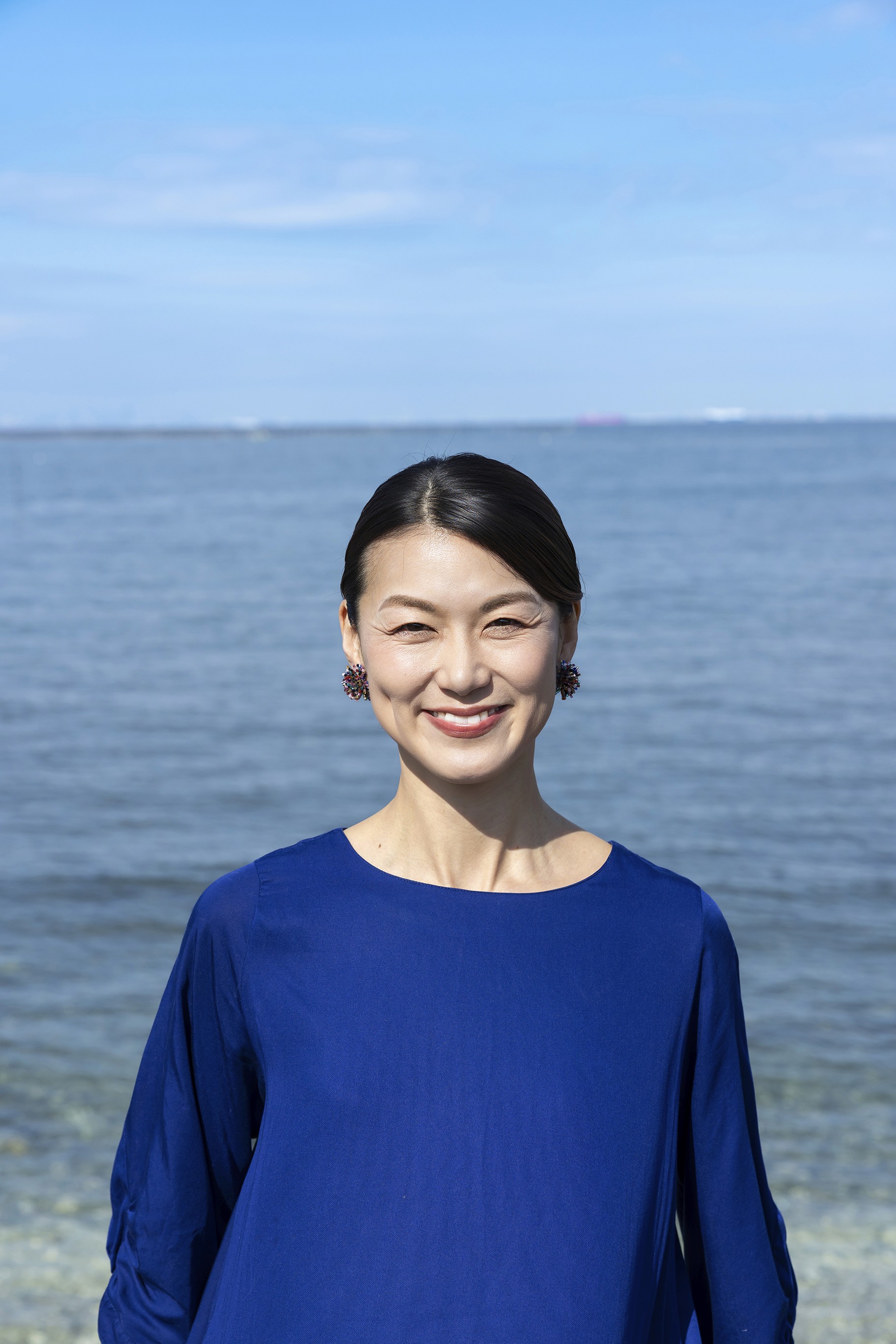 穏やかな海辺を背景に、三好智子が自然な笑顔で立っている様子。爽やかな青空と海が印象的なポートレート