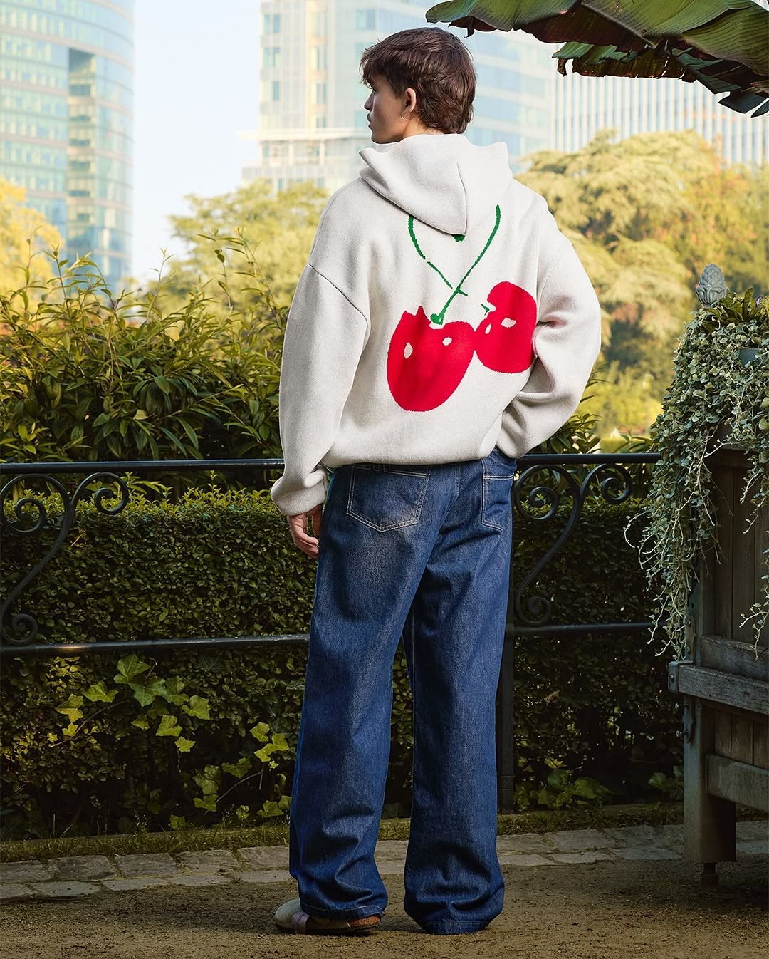 Vu de dos dans un jardin d'un mannequin portant un sweat à capuche blanc Arbor Antwerpen avec un motif de cerise